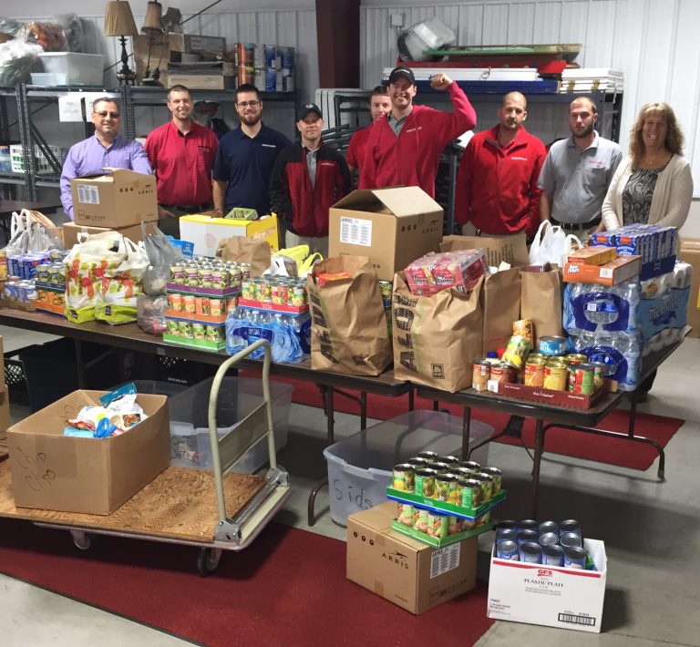 Group of volunteer workers standing behind a table that is stacked up with non-perishable food items.